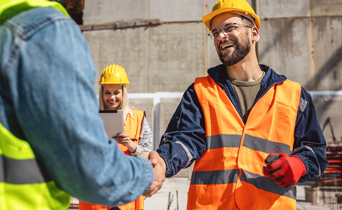 Two construction workers shaking hands at a construction site, representing collaboration in selecting a custom home builder.