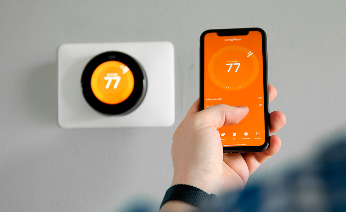 Individual using an iPhone to control a Nest thermostat, highlighting smart home features.