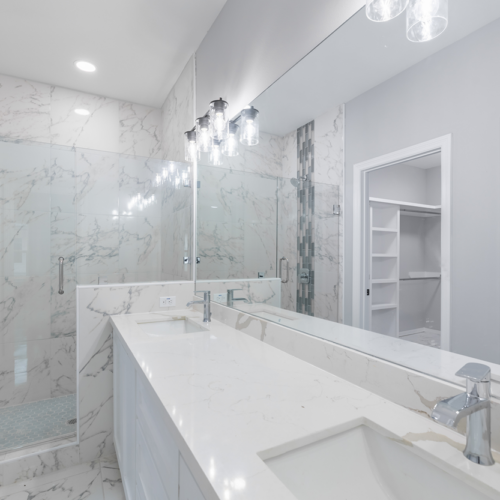 Modern bathroom with marble walls, double sink, and glass shower enclosure.