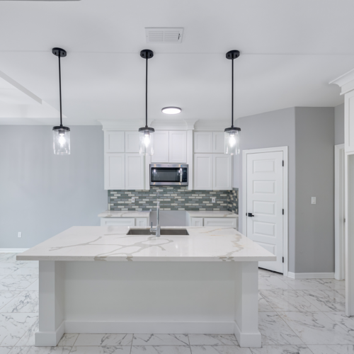 Modern kitchen featuring white cabinets, marble countertops, and stylish pendant lighting.