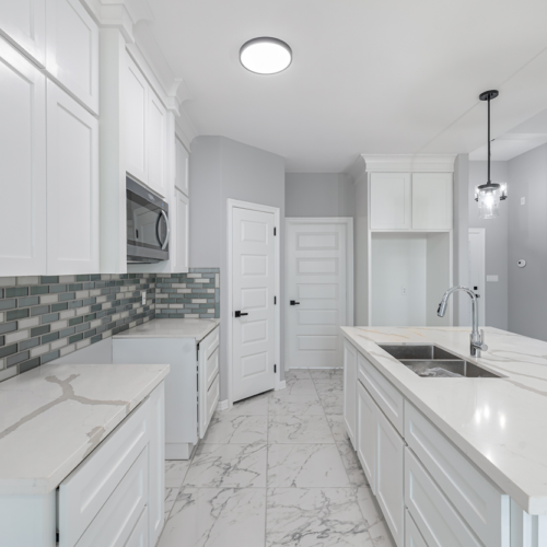 Modern kitchen with white cabinets, marble countertops, and stylish tile backsplash.